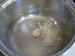 Versare in una pentola un aglio intero schiacciato e un cipollotto tritato.